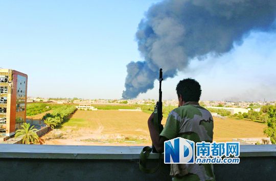 2日，利比亞首都的黎波里，一民兵武裝成員眺望被火箭彈擊中的儲(chǔ)油罐冒出濃煙。